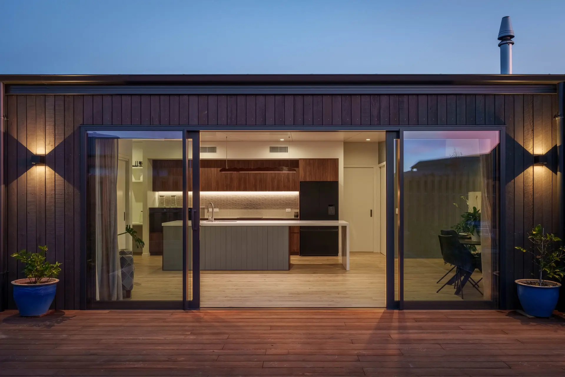 Looking from an outdoor deck into a lit kitchen at dusk
